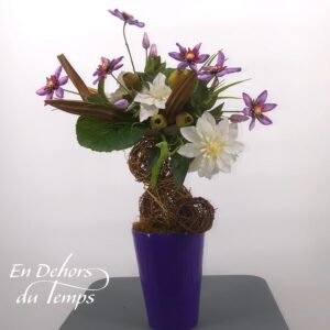 Composition florale artificielle garnie de Clématites violettes et de clématites à fleurs double blanches , d'une structure de boules en osier et de feuillage. Vase en céramique violet.