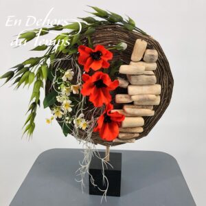 Composition florale contemporaine disque de carton sur socle en bois garni de coquelicots, fleurs blanches, feuillage et bois flotté.